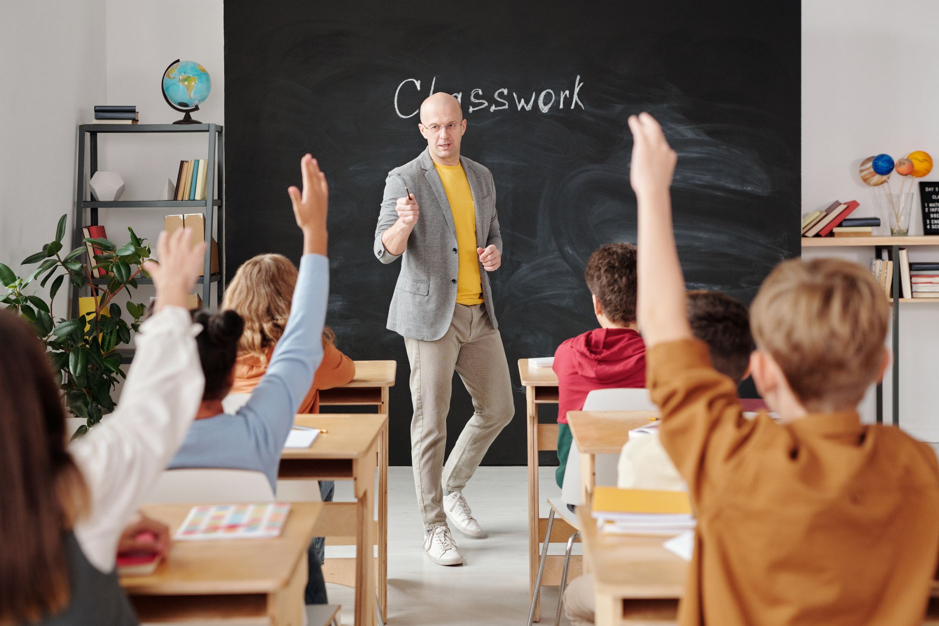 Professora conduzindo uma aula com alunos participando, de mãos levantadas