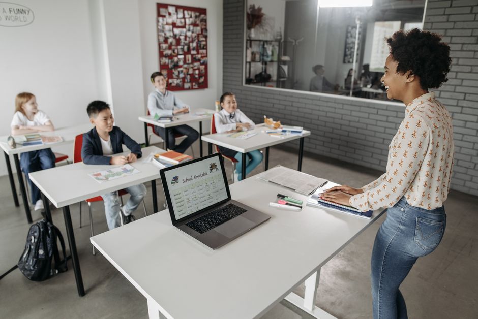 Professor interagindo com alunos em sala de aula moderna